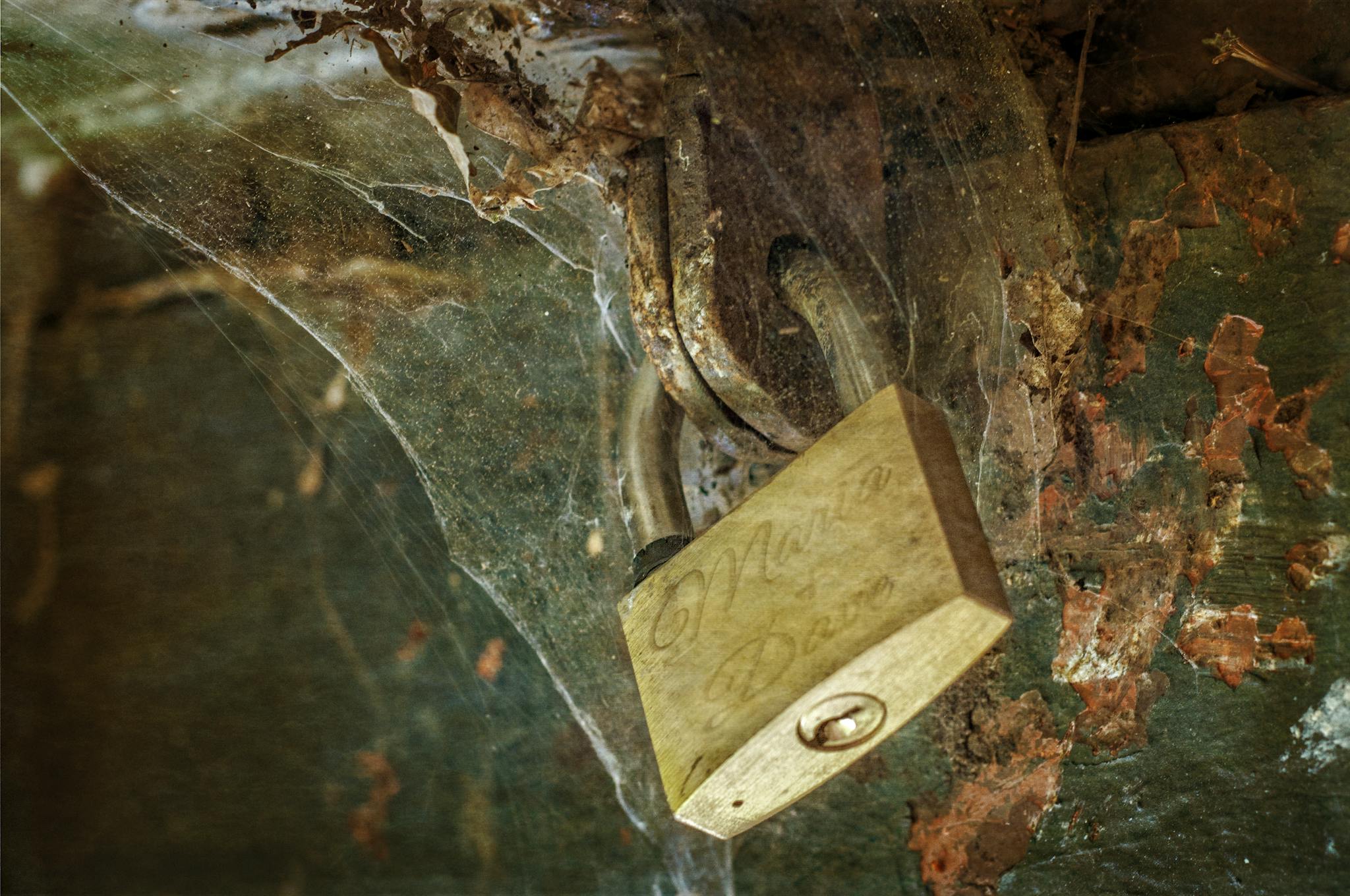 A detailed shot of a padlock surrounded by cobwebs on a rusty surface.