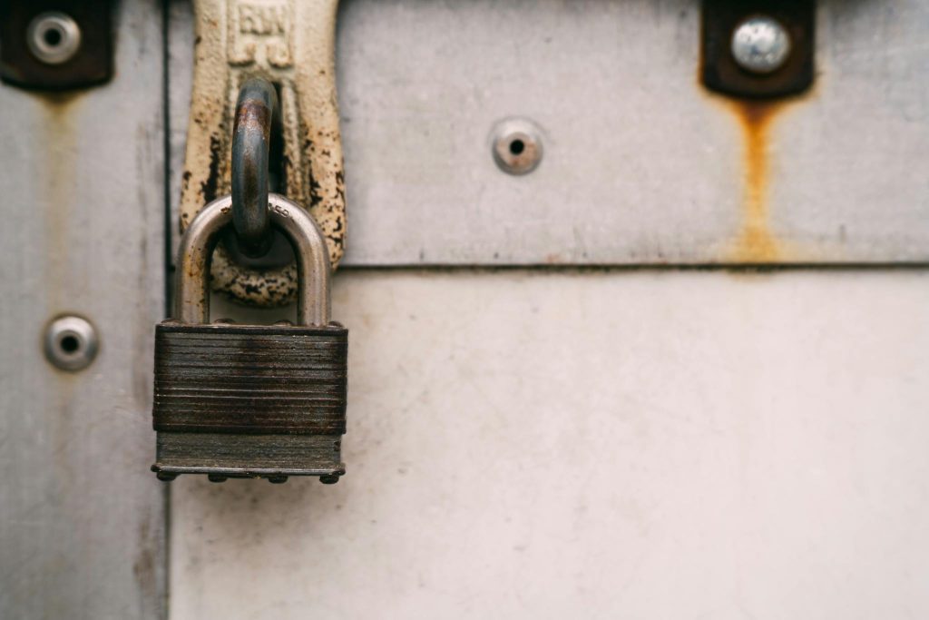 Close-up of a rusty metal padlock on a weathered door, highlighting security and decay.